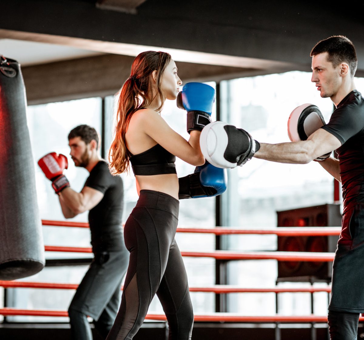 Young woman training to box with personal coach on the boxing ring at the gym