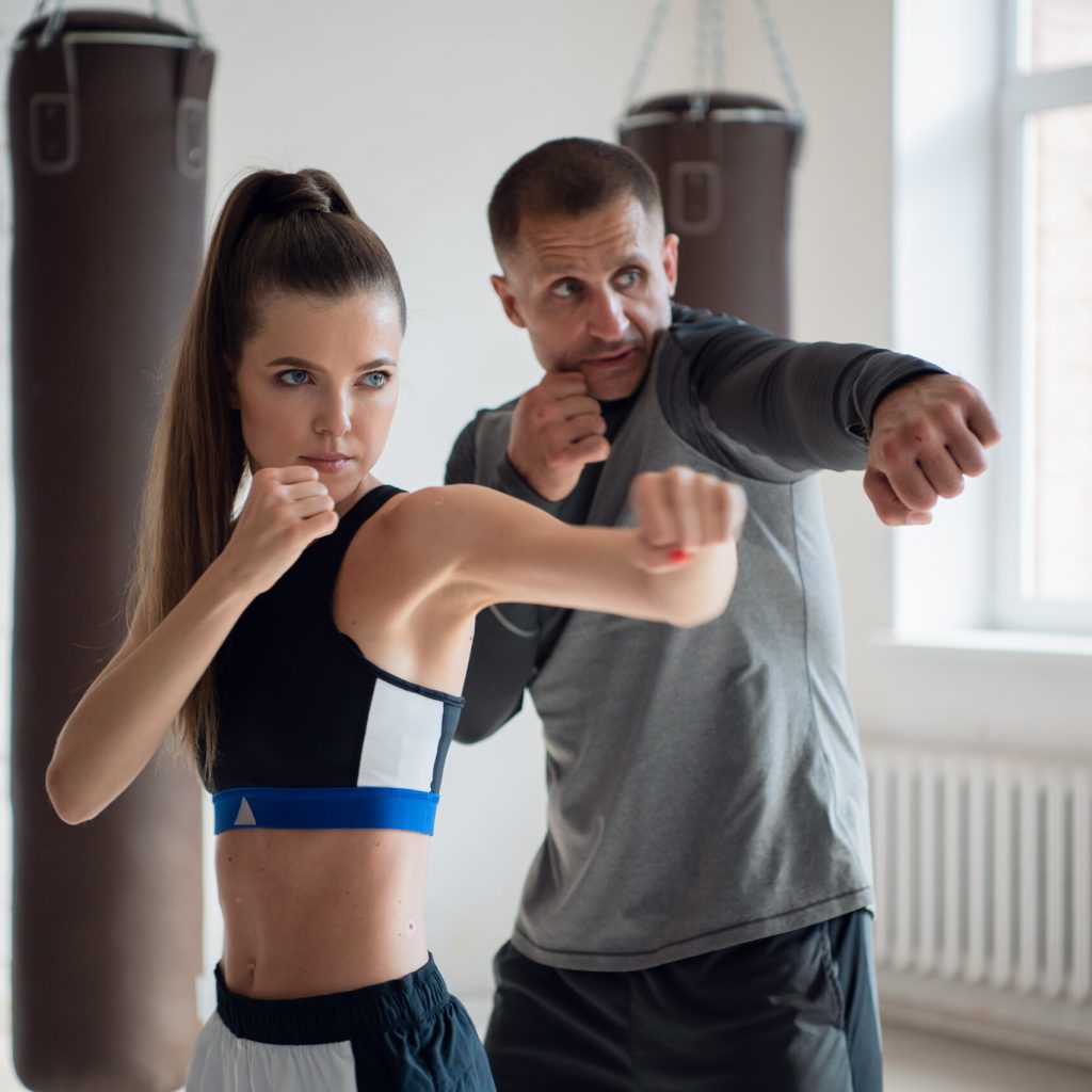 In a spacious loft, a male trainer and his female mentee conduct a boxing training session.