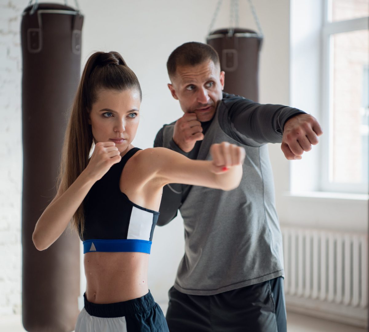 In a spacious loft, a male trainer and his female mentee conduct a boxing training session.